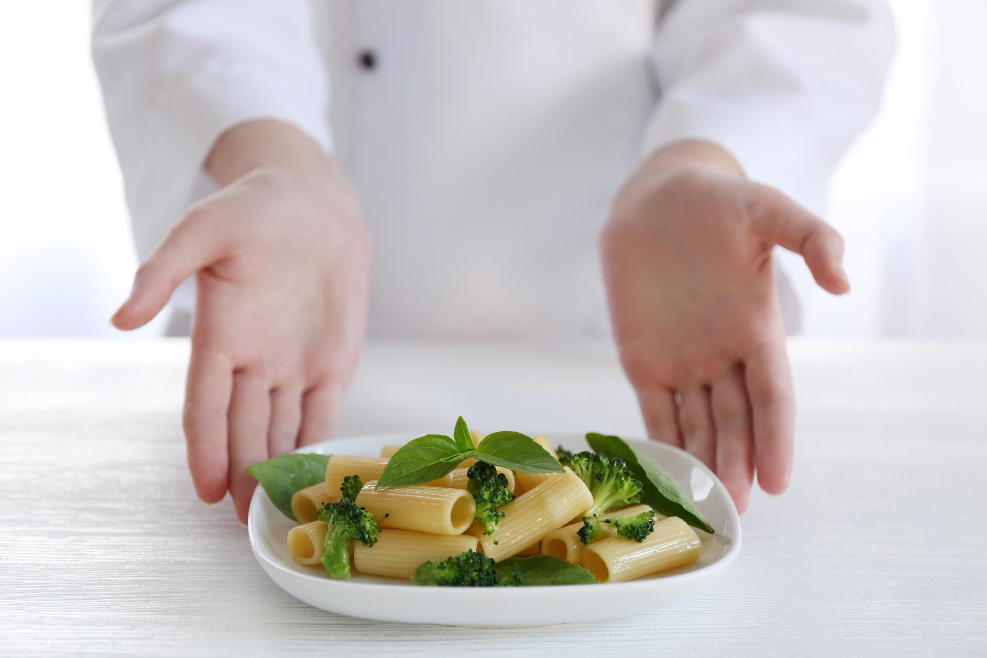 chef hands chiffonading basil over pasta