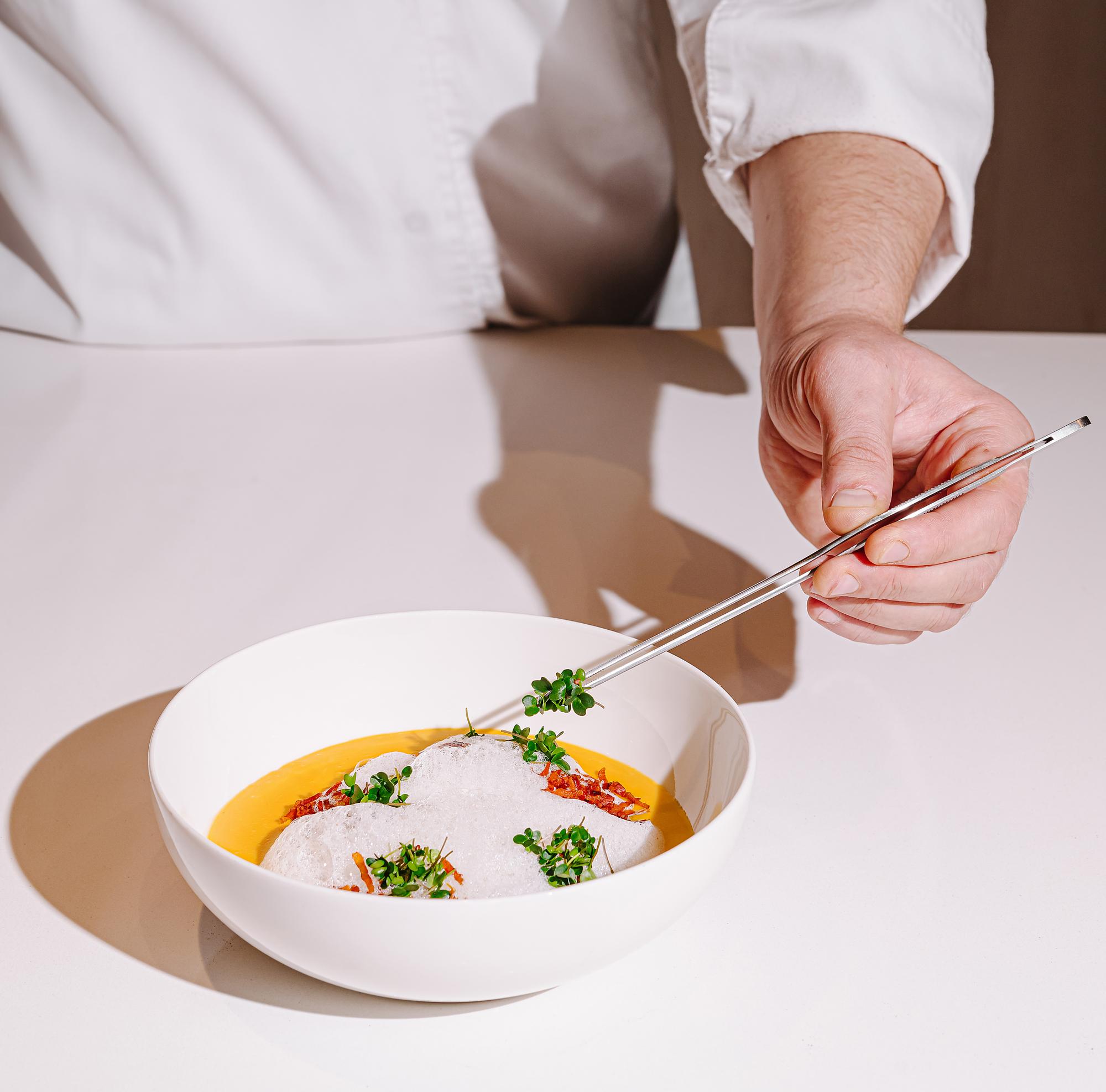 chef plating a bright modern dish on a busy counter